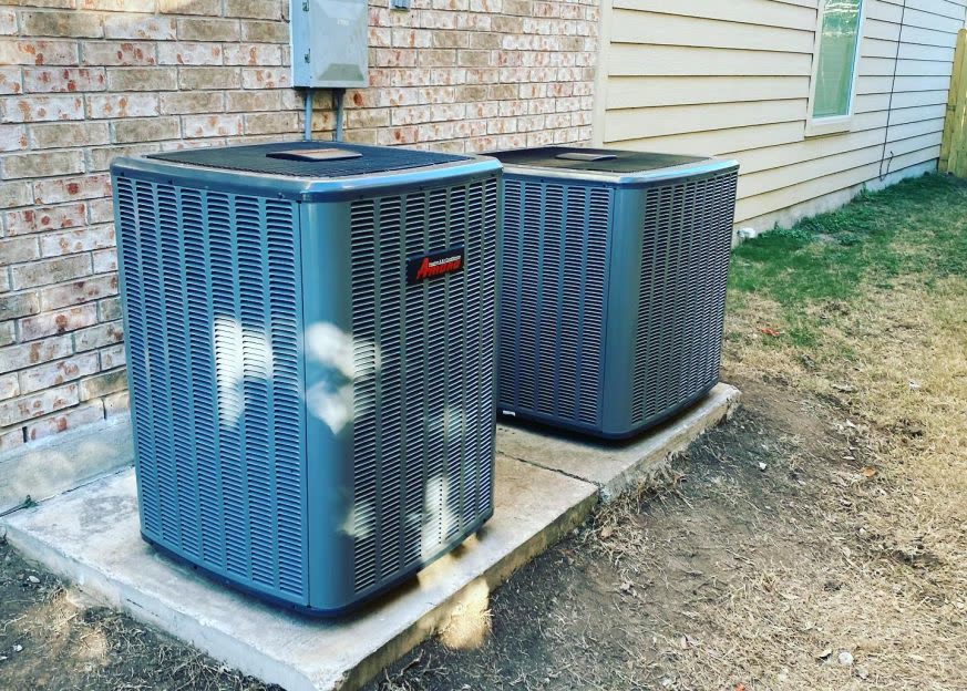 Two Amana condenser units installed side by side on a concrete pad